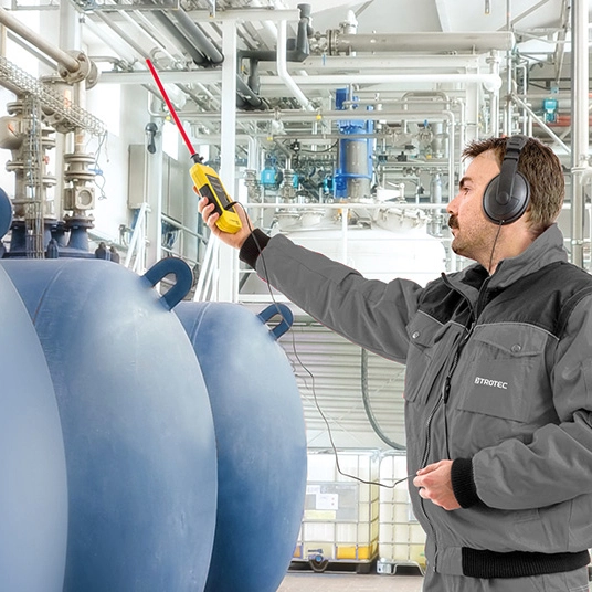 Technicien utilisant un détecteur ultrasonique pour localiser une fuite sur une canalisation industrielle