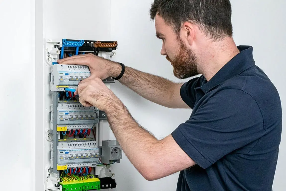 Électricien inspectant un tableau électrique résidentiel pour vérifier la conformité de l’installation.